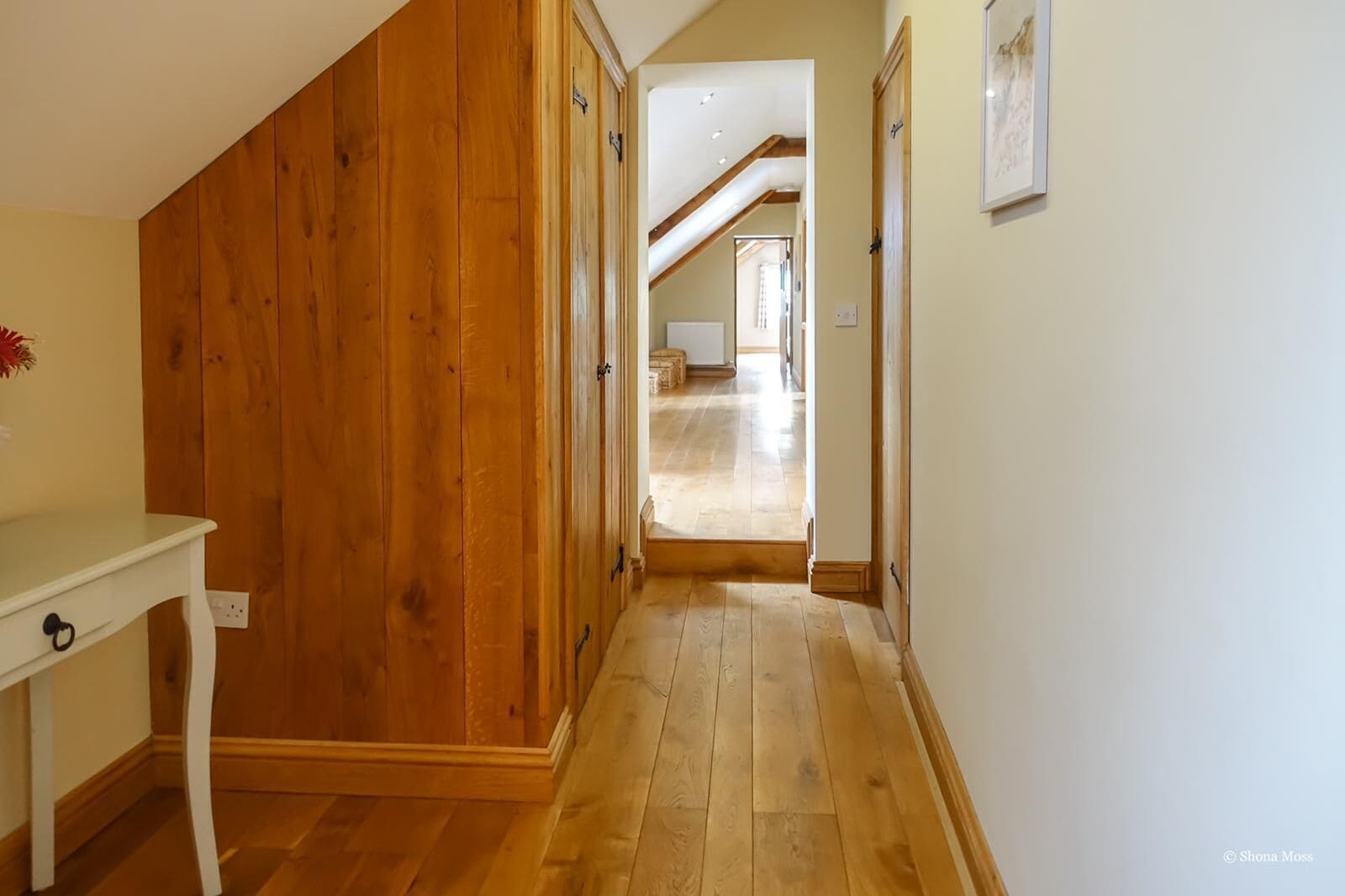 Un pasillo con suelo de madera y paredes que conduce a una habitación con ventana y puerta.