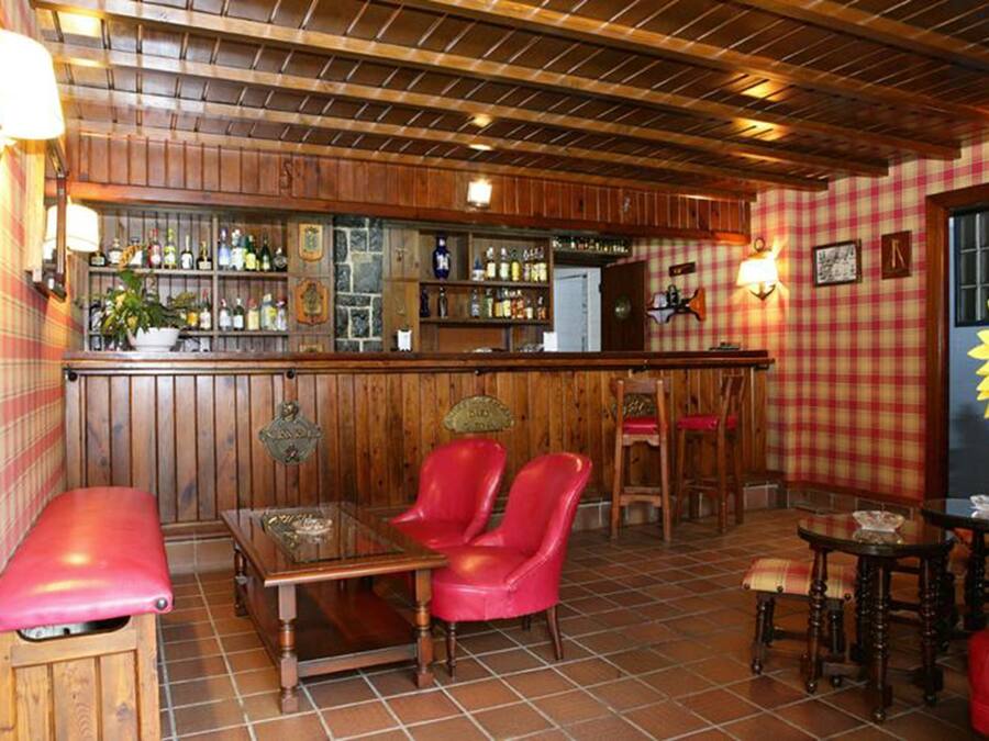 Una zona de bar con paneles de madera, una barra con botellas, sillas de cuero rojo y una pared a cuadros.
