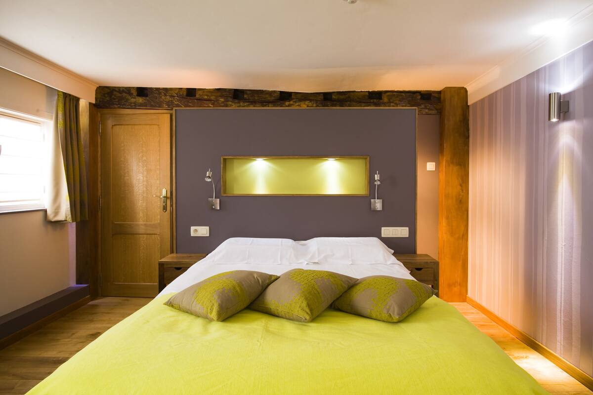 A bedroom with a bed, wooden headboard, a wall-mounted light, and a door.