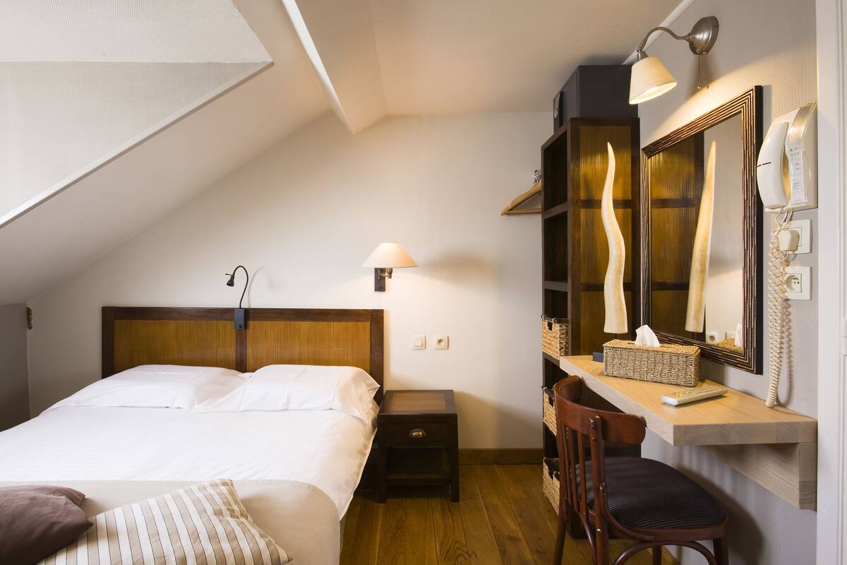 A bedroom with a bed, bedside lamp, nightstand, desk with chair, and a large mirror.