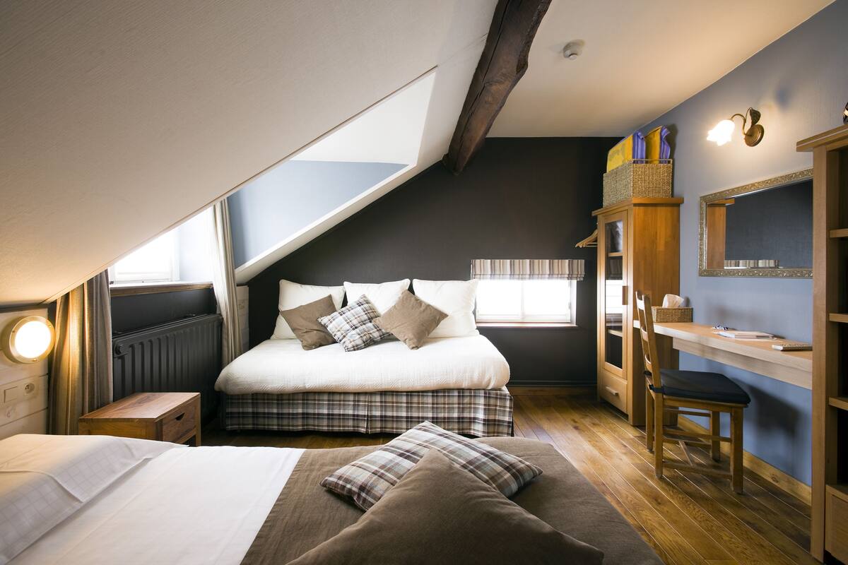 A bedroom with a loft bed, a desk, and a chair. There is a window providing natural light and a view of the outdoors.