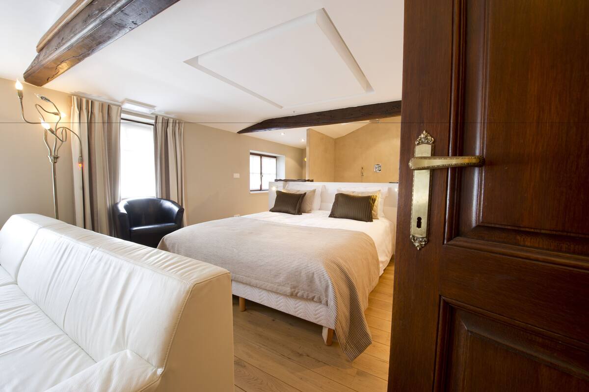 A hotel room with a large bed, a sofa, a chair, and a wooden door.