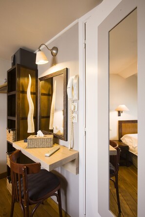 A hotel room with a wooden desk, a chair, a mirror, a lamp, a telephone, and a bedside table with a lamp. - Auberge du Sabotier (Saint-Hubert)