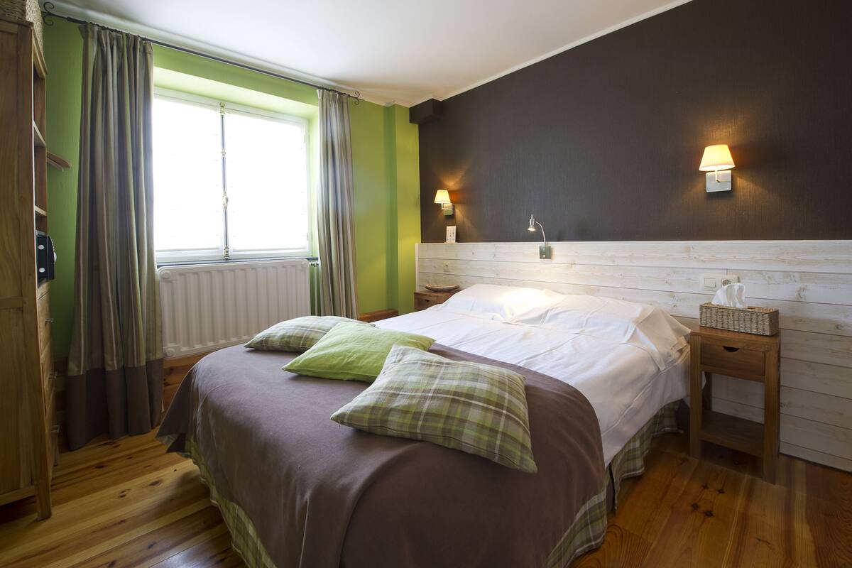 A bedroom with a bed, a nightstand, a lamp, and a window with curtains.
