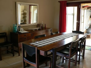 Uma sala de jantar com uma mesa de madeira, cadeiras, um espelho e uma cortina vermelha.