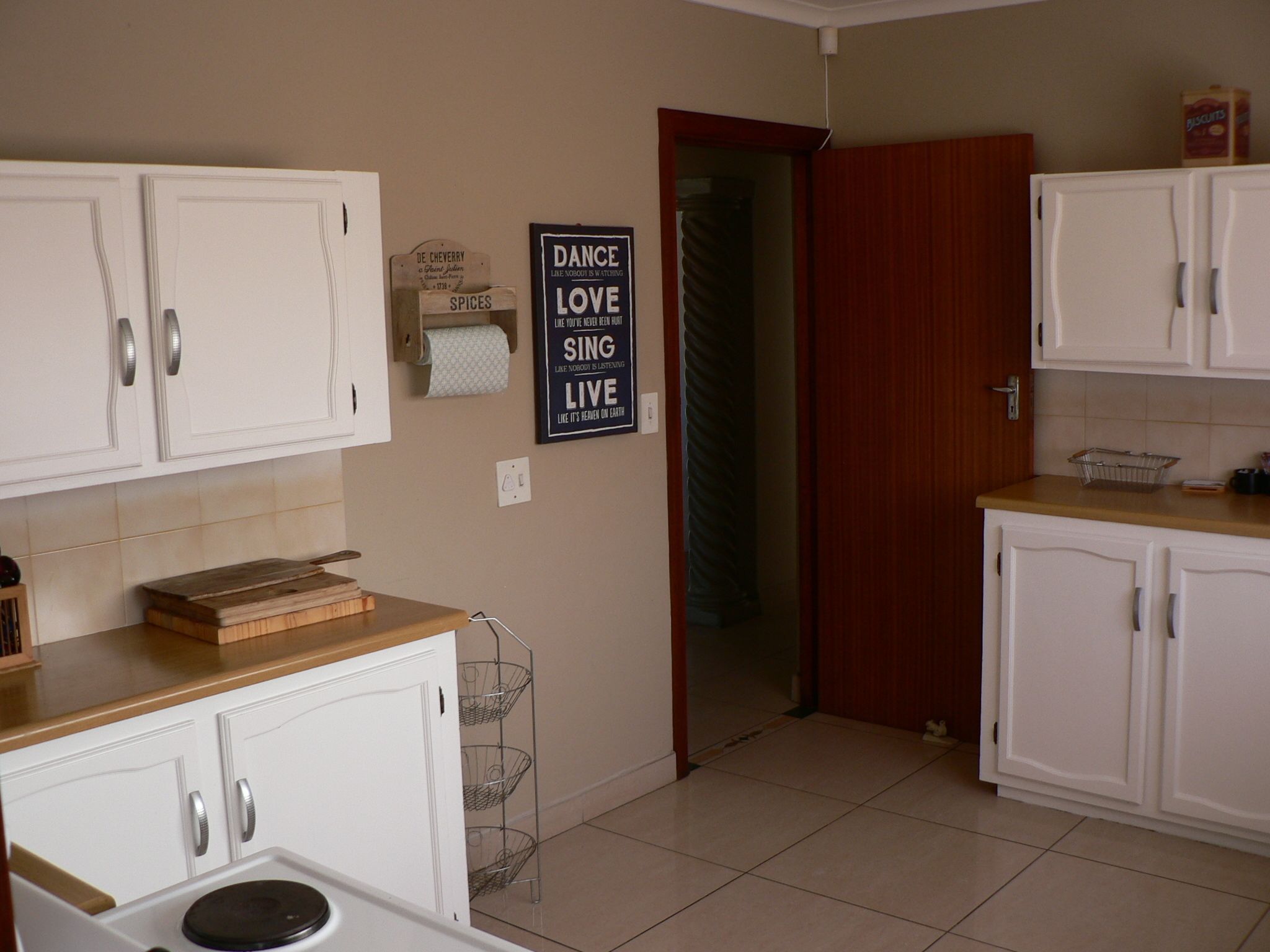 Una cocina con armarios blancos, encimera de madera y estante para especias fijado a la pared.