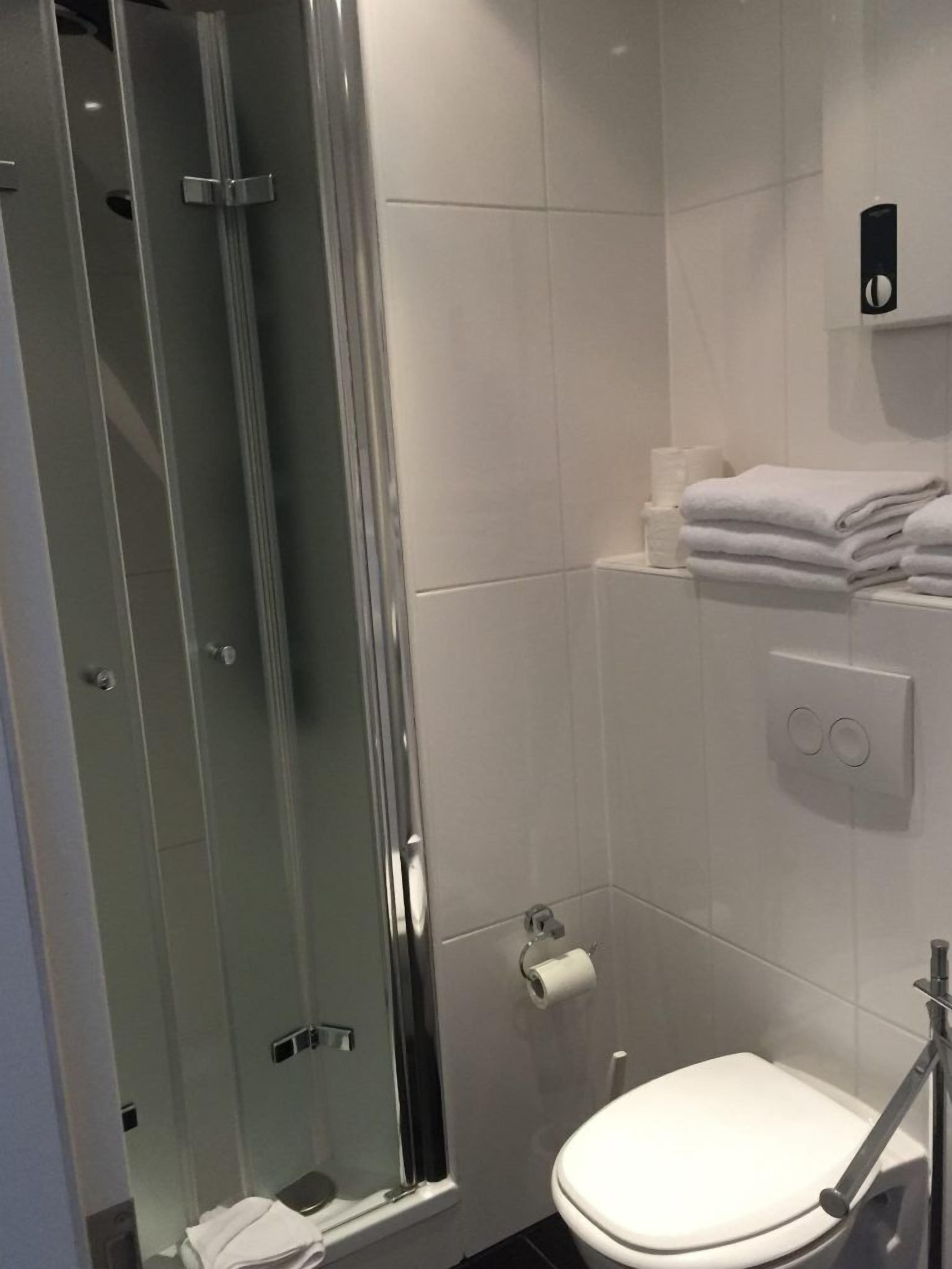 A bathroom with a glass-enclosed shower, a toilet, and a towel rack with folded towels.