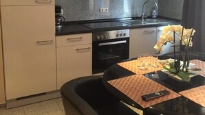 A compact kitchen with a stove, oven, and modern cabinetry. There is a dining area with a table set for two, featuring a vase with flowers. - Pension Am Zollverein (Essen)