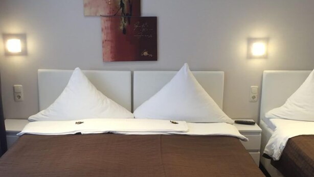 A hotel room with a large bed, two bedside tables, and wall-mounted artwork. - Pension Am Zollverein (Essen)