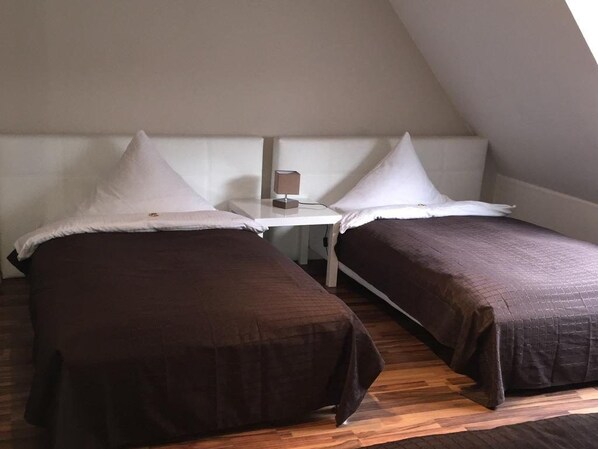 Two single beds with white pillows and brown bedspreads in a room with a sloped ceiling and wooden flooring. - Pension Am Zollverein (Essen)