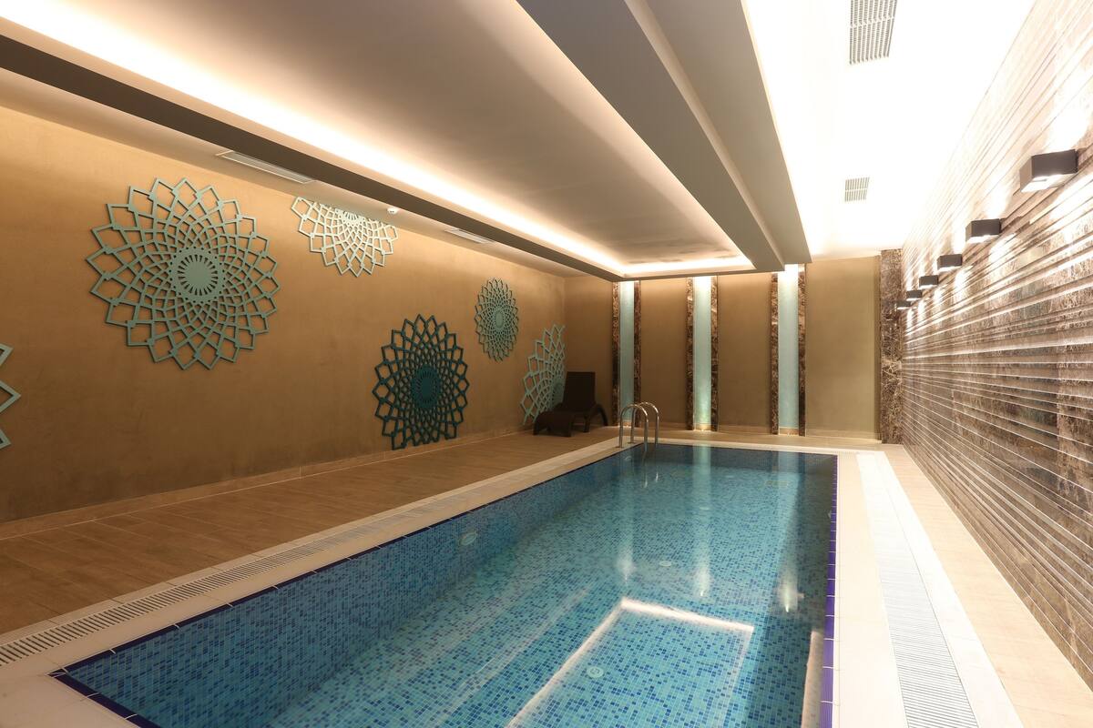 Ein Schwimmbecken mit geometrischen Wandverzierungen, Fliesenboden und modernem Deckenstil.