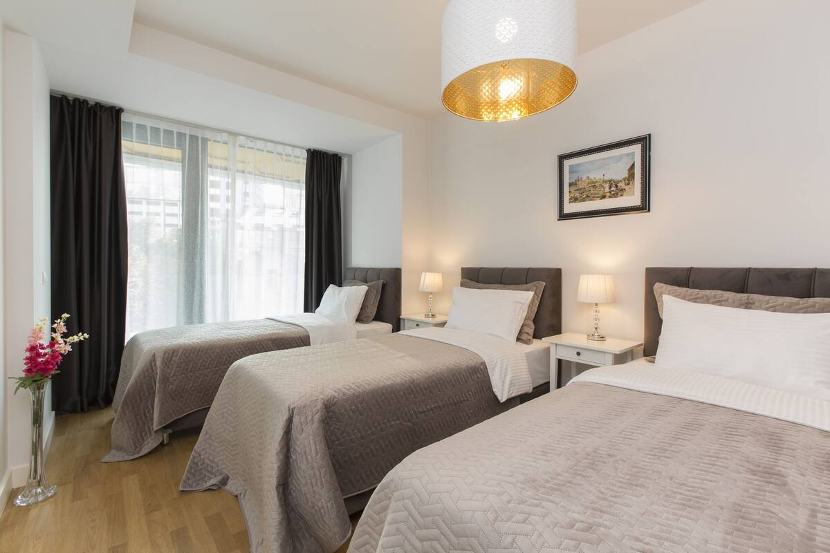 Ein Hotelzimmer mit zwei Betten, einem Nachttisch mit Lampen, einem Bild an der Wand und einem Fenster mit Vorhängen.
