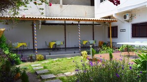 An outdoor patio area with tables and chairs, surrounded by potted plants and a small garden. - Hôtel Saint-Jean (Cotonou)