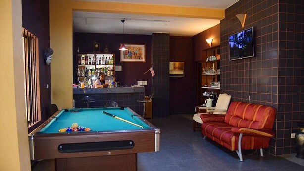 A pool table in a room with a bar and a red couch. - Hôtel Saint-Jean (Cotonou)