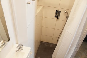 A small, modern bathroom with a white sink, a shower, and a toilet.
