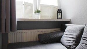 A corner room with a grey sofa, a window with white shutters, a small plant, and a black lantern on the windowsill. - Noctis Apartment Chmielna (Warsaw)