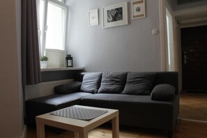 A modern living room with a grey sofa, a small wooden table, and a window with curtains.