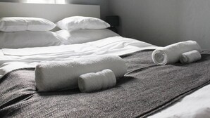 A neatly made bed with white linens and rolled towels, a gray textured blanket, and a bedside table with a lamp. - Noctis Apartment Chmielna (Warsaw)