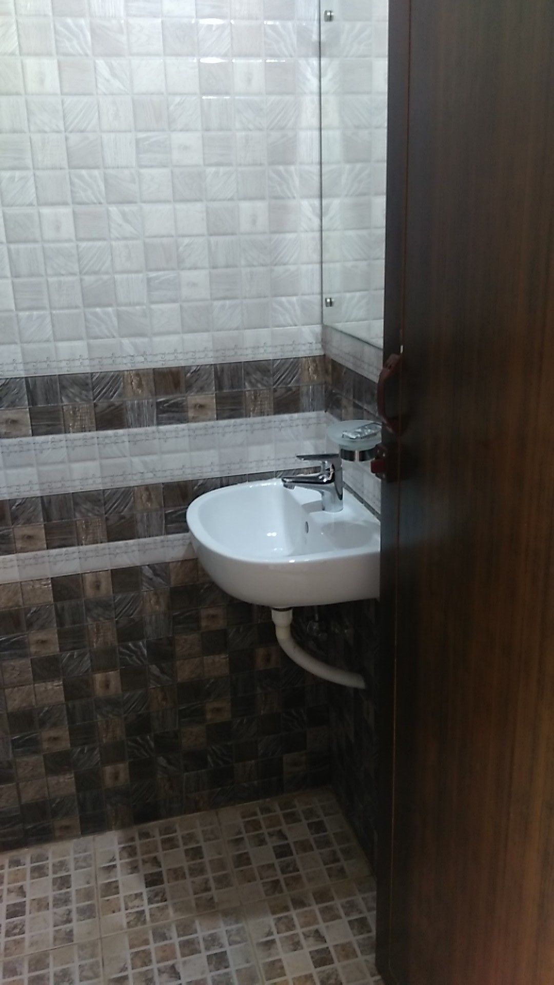 A bathroom with a white sink, dark patterned tiles, and a wooden door.