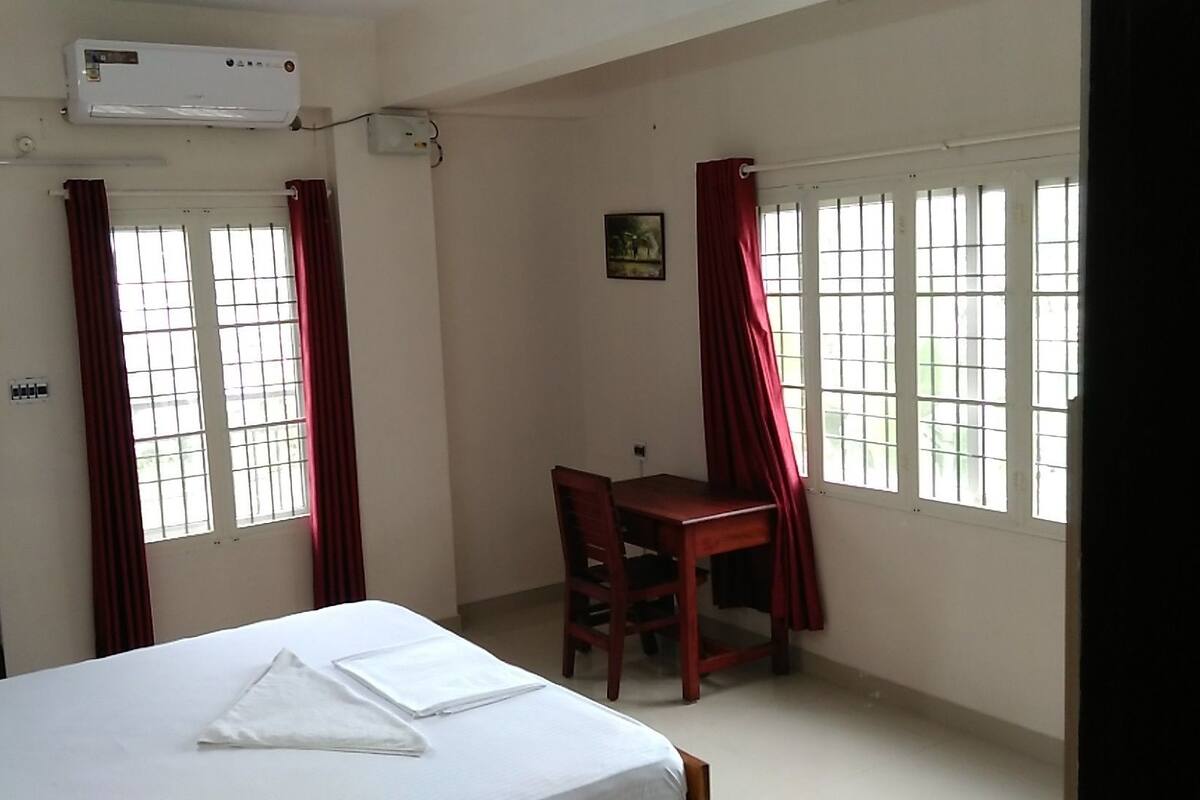 A hotel room with a bed, a desk, and two windows with red curtains.