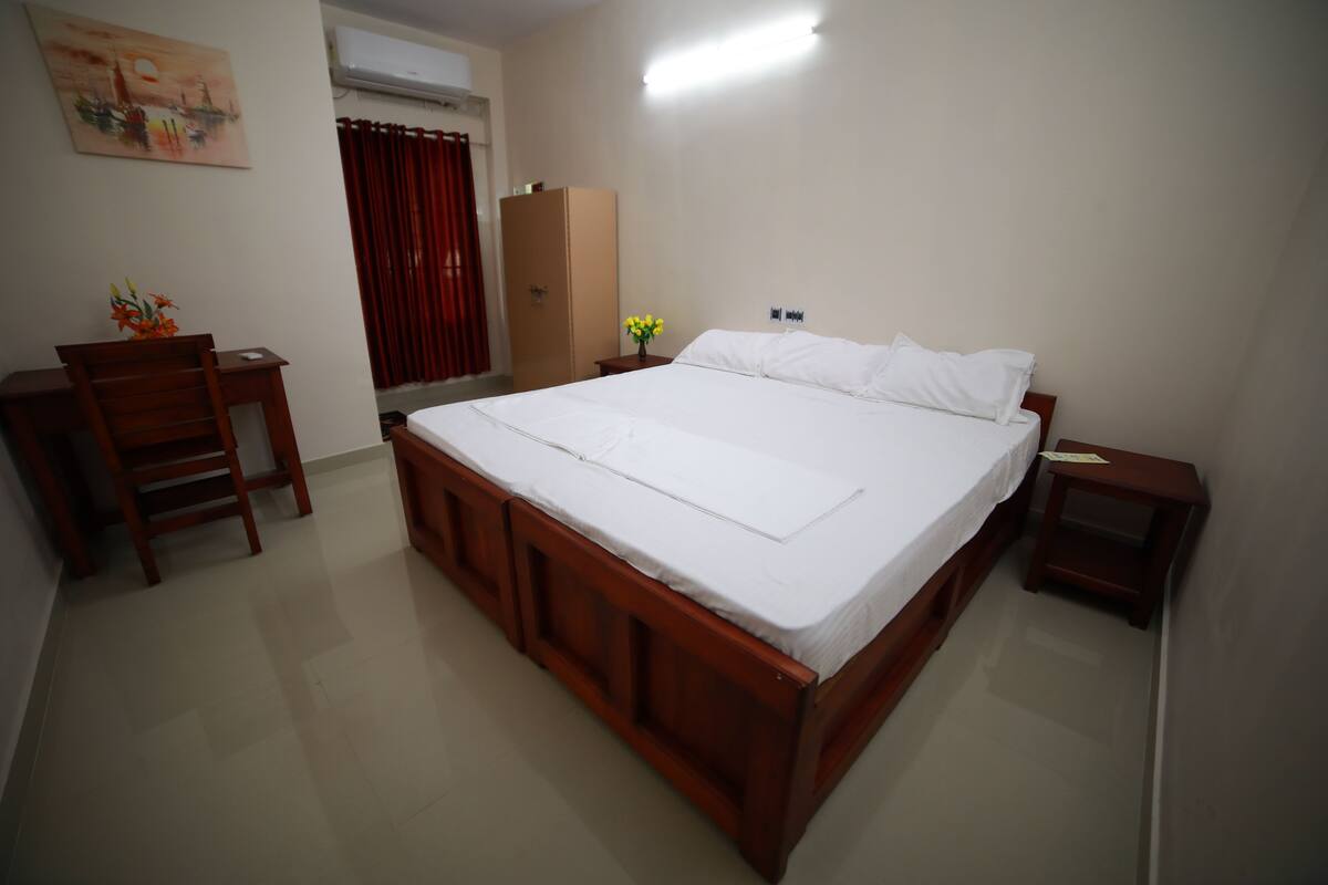 A bedroom with a wooden bed, a desk, a chair, a wardrobe, and a nightstand.