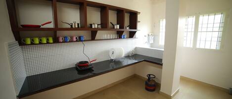 A kitchen with a black countertop, white tiled backsplash, and wooden shelves.