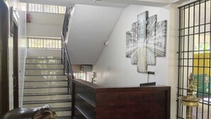 A reception area with a staircase, a wooden reception desk, a wall-mounted artwork, and a brass lamp. - Indeevaram Residency (Thiruvananthapuram)