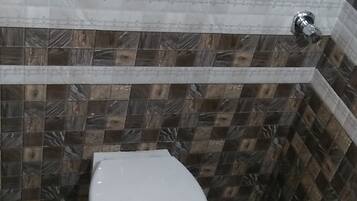 A small bathroom with a white toilet, tiled walls, and a shower area.
