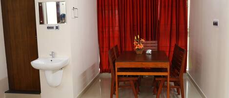 Una habitación con puerta de madera, un lavamanos blanco, un espejo, una cortina roja y una mesa de comedor con sillas.