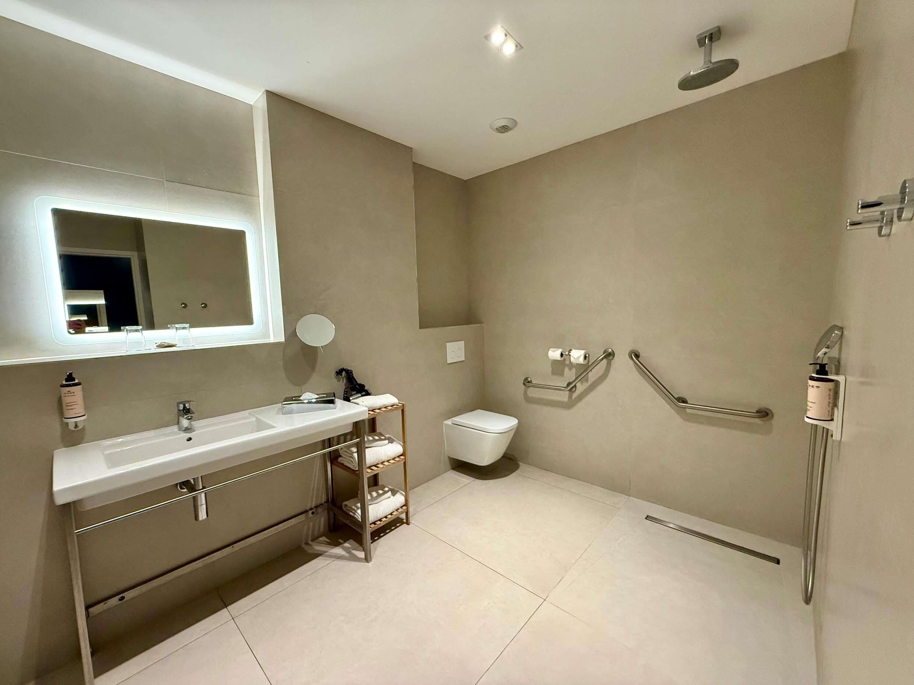 Un baño moderno con un espejo grande, lavamanos, inodoro y zona de ducha.