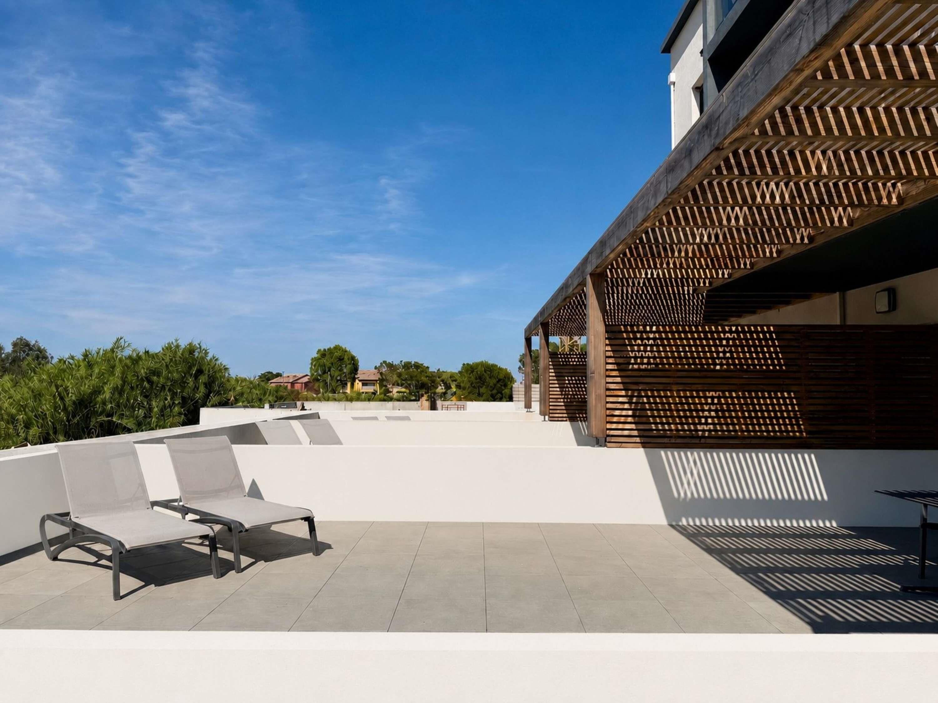 Una terraza en la azotea con mobiliario exterior y una pérgola de madera.