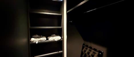 A dark room with a shelving unit containing folded towels and a chair.