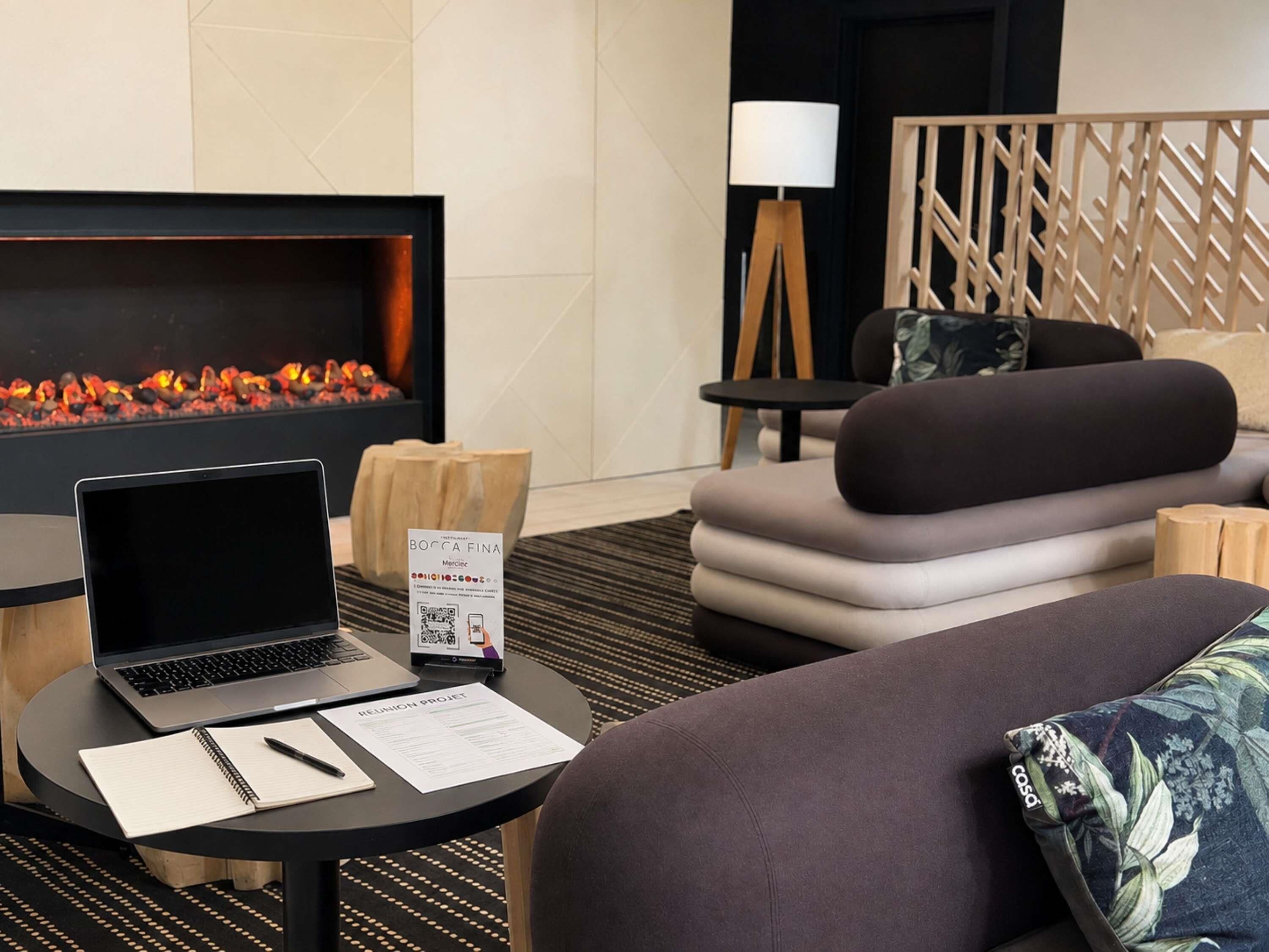 Una habitación de hotel moderna con chimenea, una laptop sobre una mesa, un sofá y un panel decorativo en la pared.