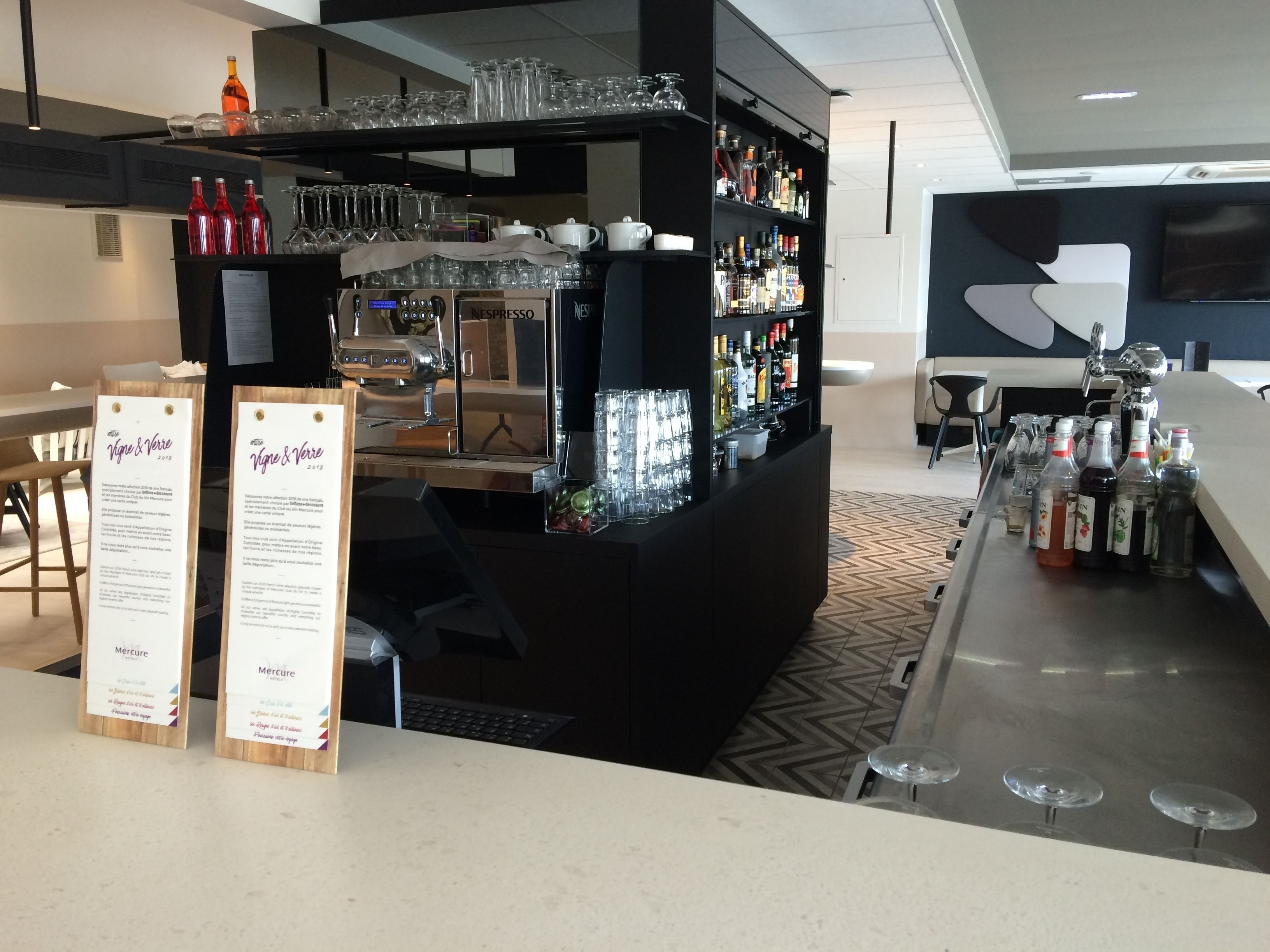 A bar area with a Nespresso machine, shelves of liquor bottles, and a menu stand.
