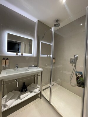 Un baño moderno con ducha envuelta en vidrio, tocador con espejo y perchero para toallas.
