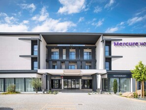 Un hotel moderno con restaurante, que destaca por una entrada limpia, grandes ventanales y un cielo despejado.