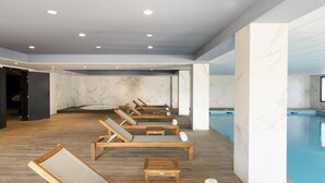 Ein Wellnessbereich mit Holzliegen, einem Pool, Marmorwänden und eingelassenen Deckenleuchten.