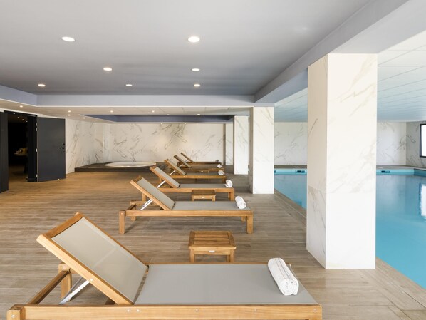 A spa area with wooden loungers, a pool, marble walls, and recessed ceiling lights. - Mercure Hotel & Spa Bastia Biguglia (Biguglia)