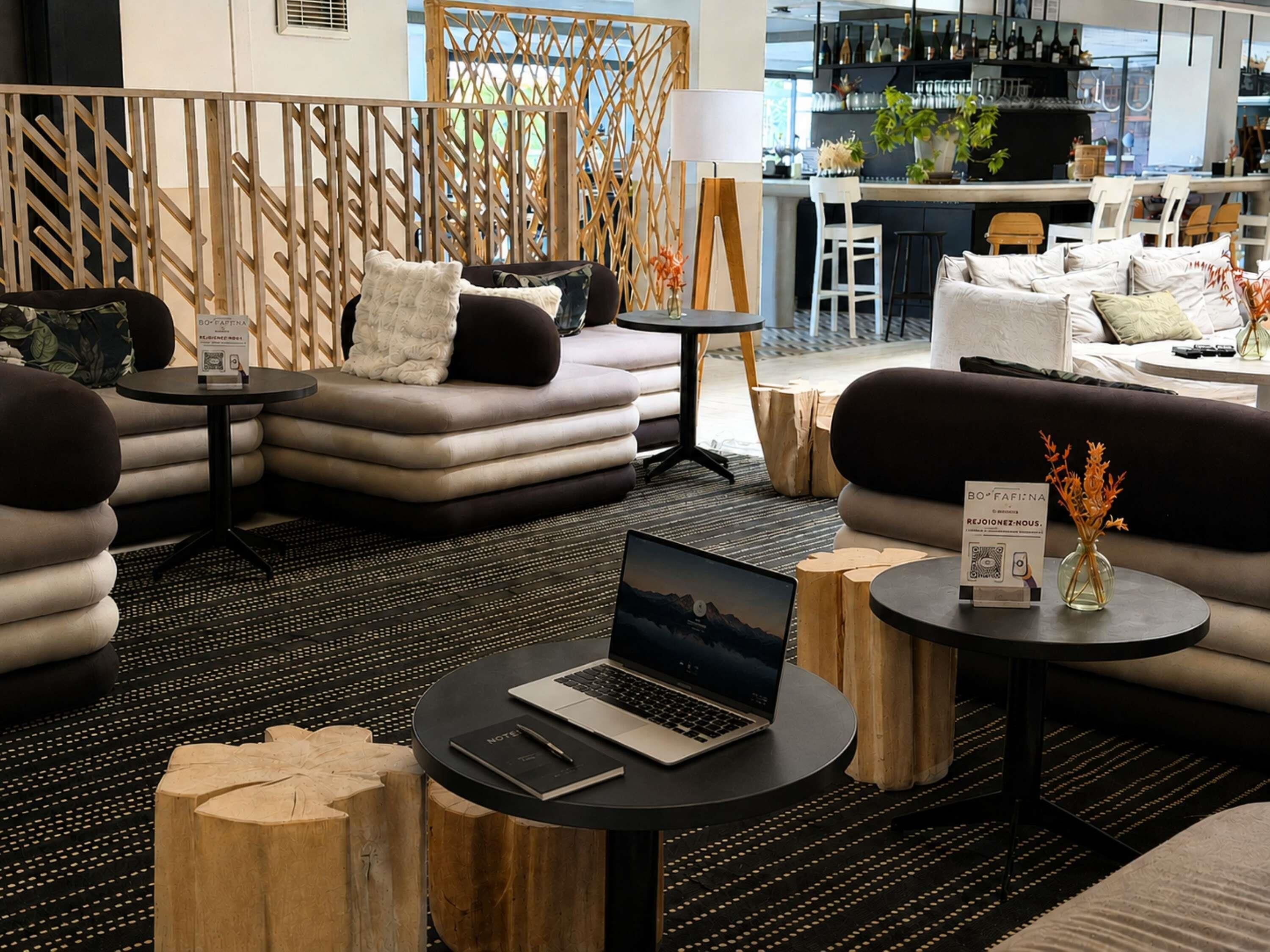A modern lounge area with sofas, a laptop on a table, and a bar in the background.