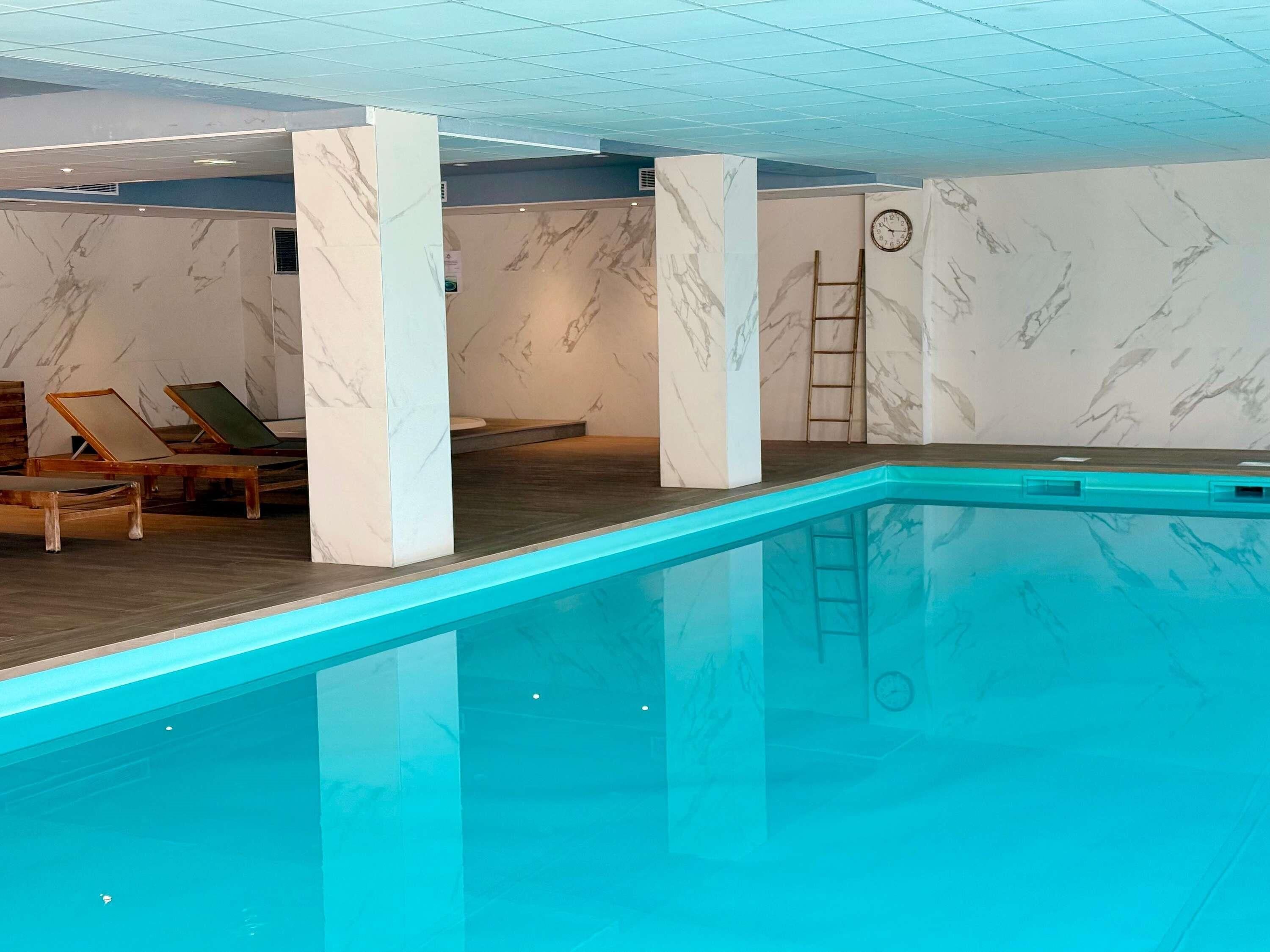Une piscine dotée d’une terrasse en bois, de murs en marbre et d’une échelle.
