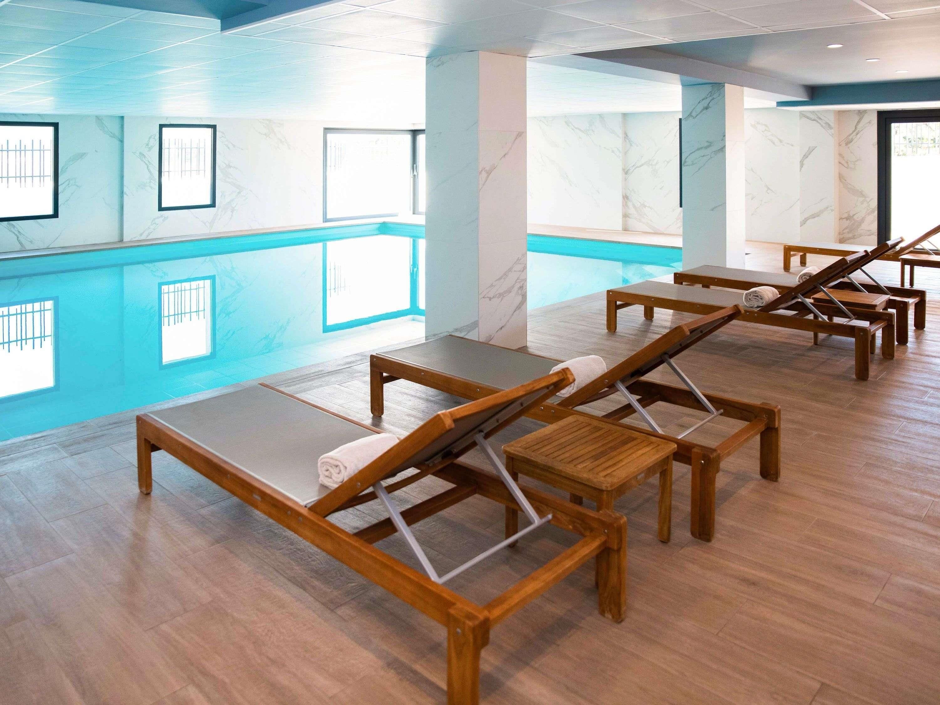 A modern indoor pool area with wooden loungers and a clear view of the pool.