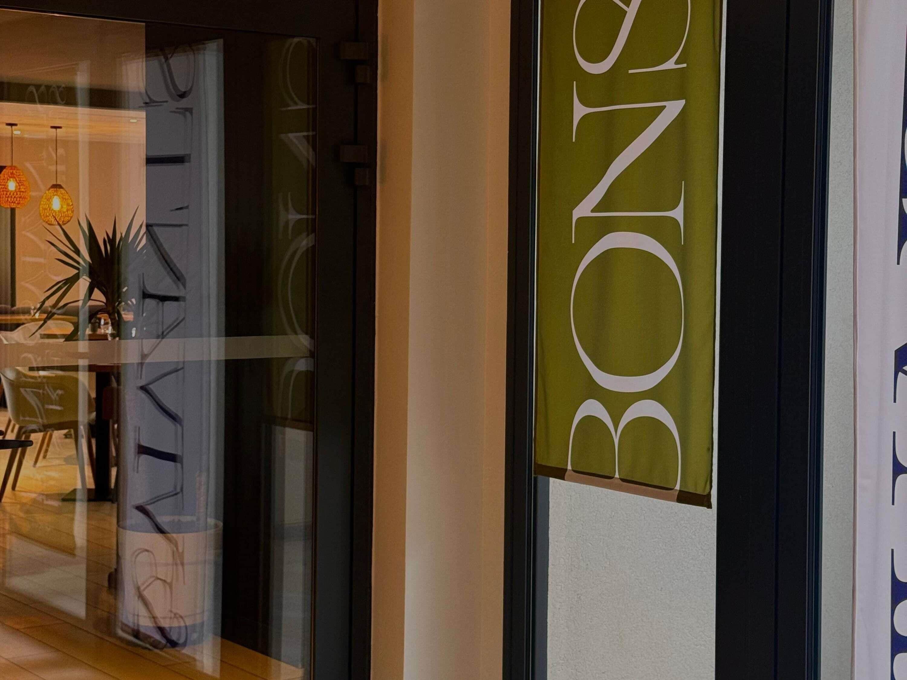 L’intérieur d’un hôtel avec une porte en verre, un espace salon bien visible avec des chaises, et une enseigne portant le nom « BONBON ».