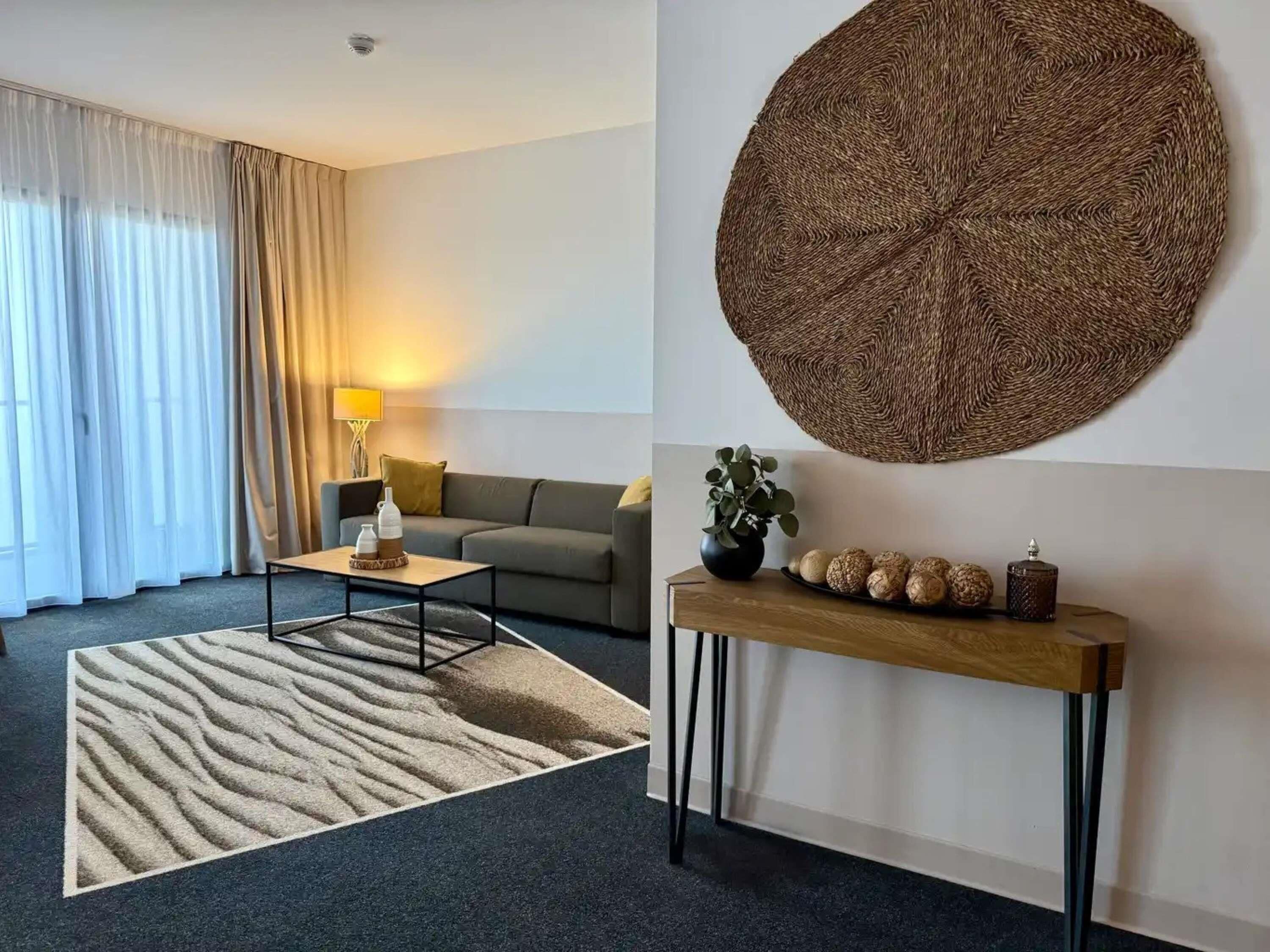 Una sala de estar moderna con un sofá, una mesa de centro, un tapete, una consola decorativa y un gran tapiz tejido.
