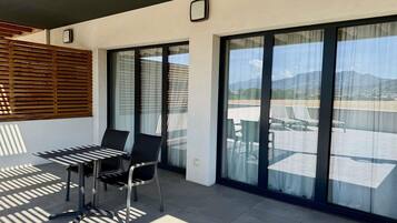 Ein Balkon mit Tisch und Stühlen, große Schiebeglasfenster und Blick auf eine gebirgige Landschaft.