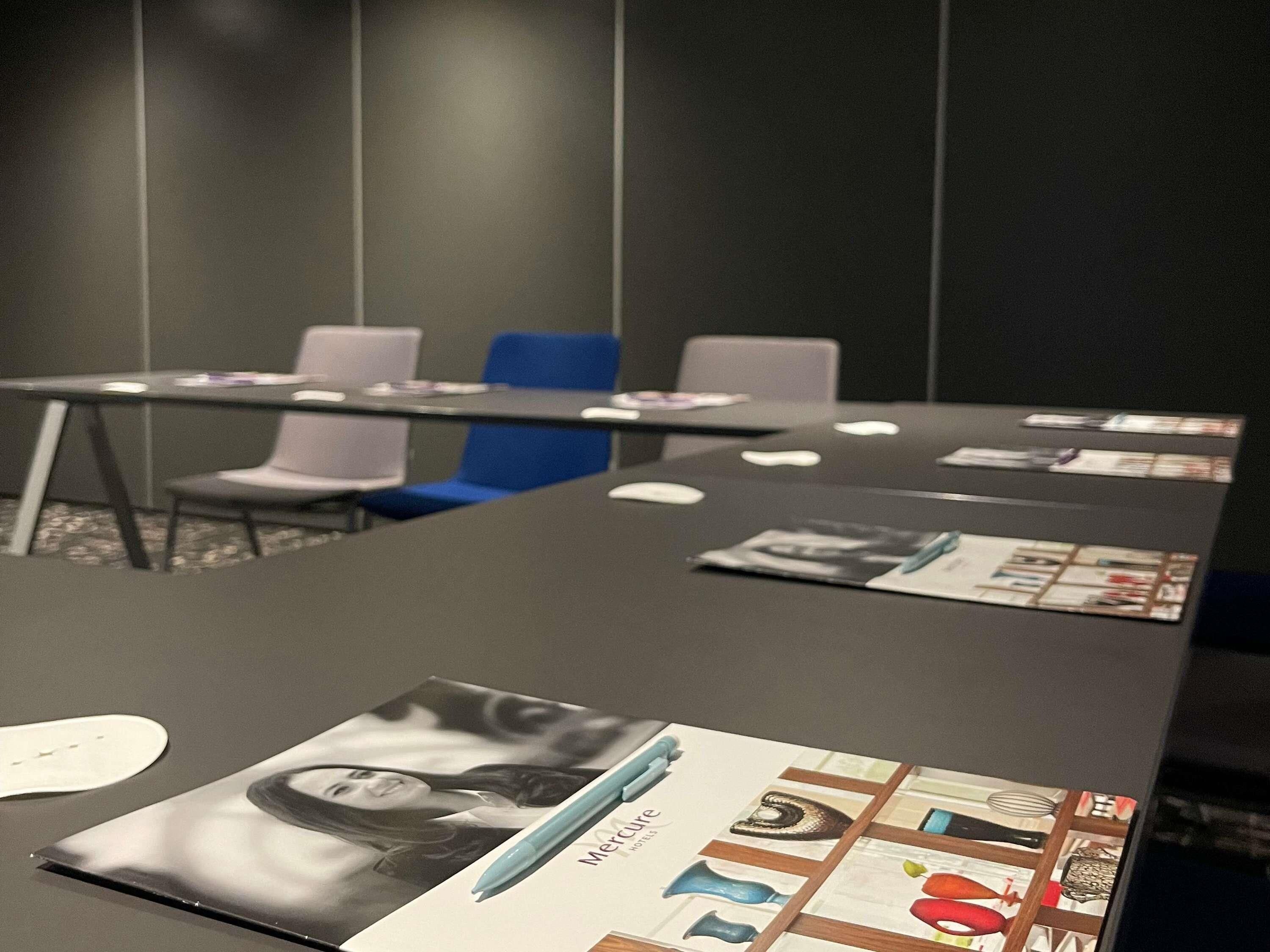 Un salón de conferencias con una larga mesa, varias sillas y folletos informativos.