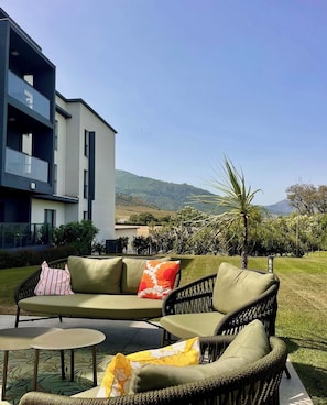 A modern outdoor seating area with a sofa and two chairs, a small table, and a view of a building and hills in the background.