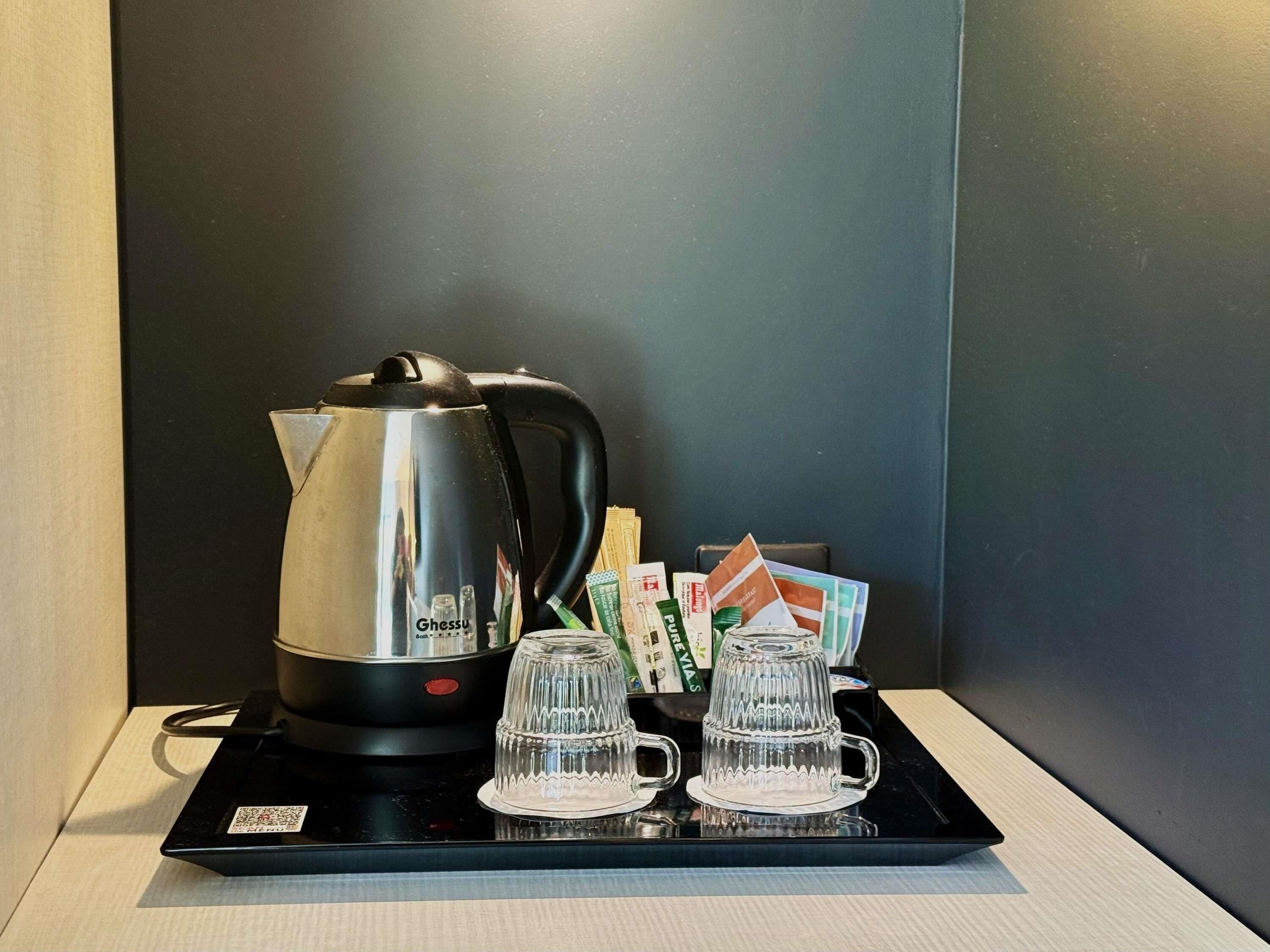 Un plateau noir sur lequel se trouvent une bouilloire électrique de la marque Gghsu, deux verres transparents et quelques cartes, le tout posé sur une table.