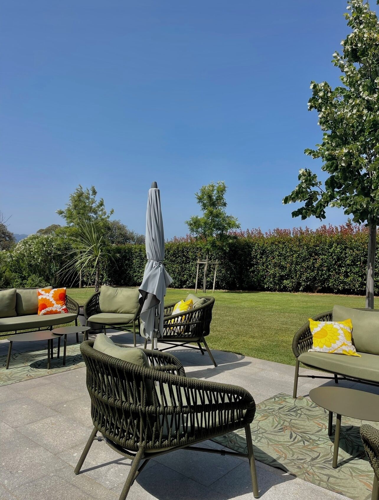 An outdoor seating area with wicker chairs, a grey umbrella, and a green sofa.