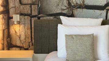 A bed with white bedding, a textured pillow, and a headboard against a wall with a stone-like texture and branches.
