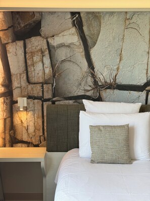 A bed with white bedding, a textured pillow, and a headboard against a wall with a stone-like texture and branches. - Mercure Hotel & Spa Bastia Biguglia (Biguglia)